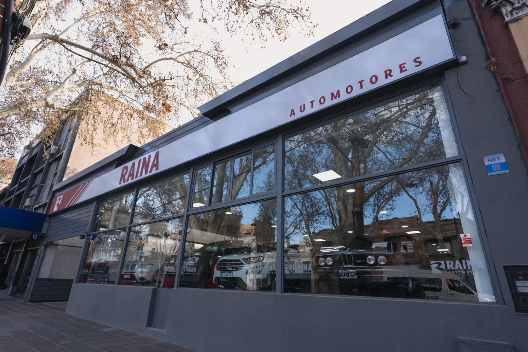 Fachada vidriada de una sucursal de Raina Automotores en Mendoza con autos en el salón